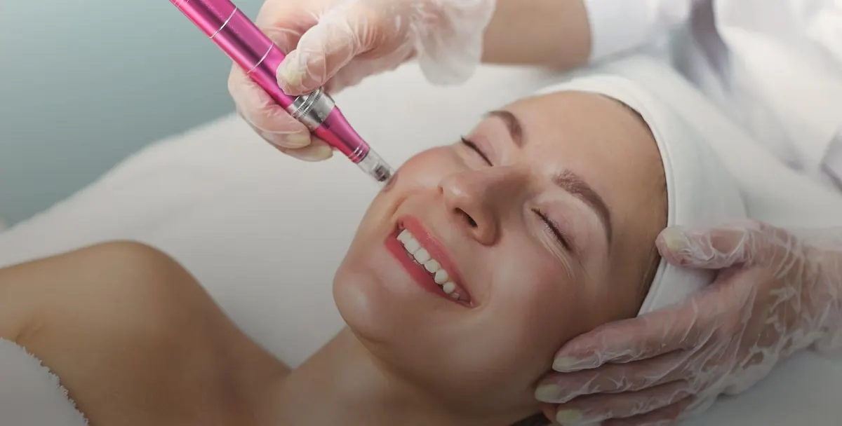 A gloved therapist using a microneedling pen on the cheek during a facial treatment.