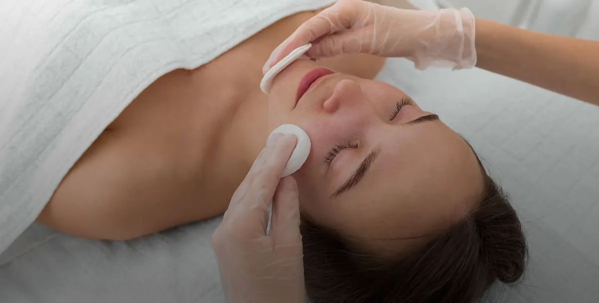 A therapist gently cleansing the cheeks with cotton pads during a facial.